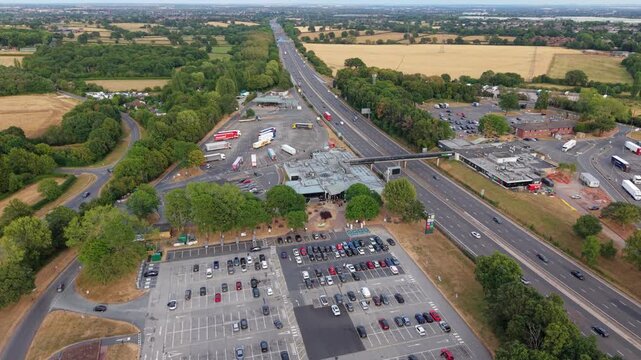 Aerial orbit view of busy motorway service station and traffic slip roads on M6 in Warwickshire UK