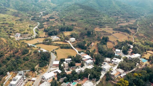 Aerial view of rural mountain village with winding road and terraced hillsides