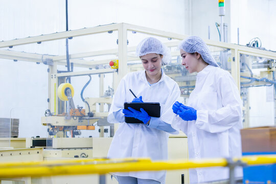 Quality control inspectors working with digital tablet in food factory plant, female factory workers checking production line, industrial production line operators inspecting manufacturing facility