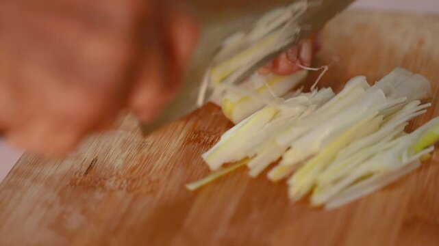 Cook slicing leek into thin strips on wooden cutting board