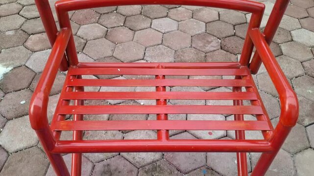 Empty orange metal swing seat moving gently swinging above paving block ground in the park playground outdoors