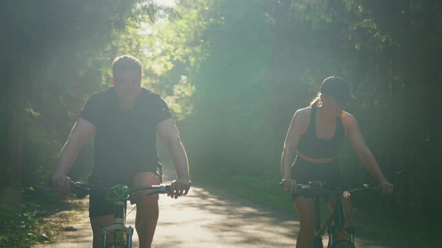 Cyclists riding together through sunlit forest trail, enjoying active outdoor fitness, healthy lifestyle, and peaceful nature scenery on a quiet paved path
