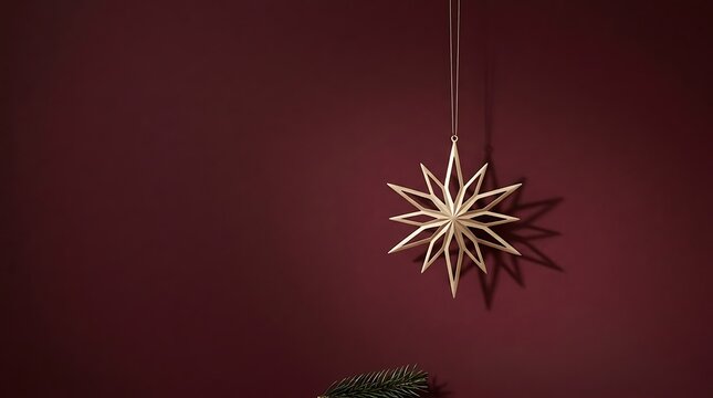 Minimalist golden star shaped christmas tree ornament hanging against a dark maroon background