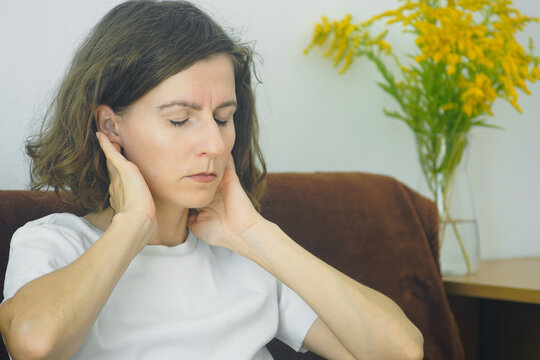 Close portrait of woman touching neck side behind ear for muscle stiffness easing. Illustrates cervical tension release technique, somatic therapy practice, and trigger point discomfort alleviation.