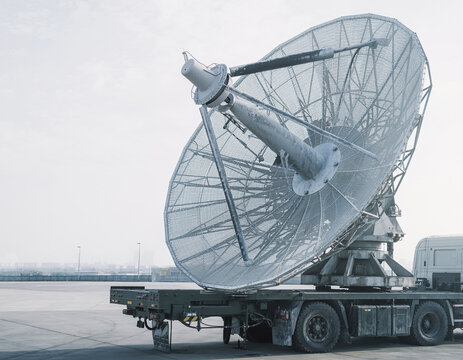 A large parabolic antenna on a heavy truck chassis, featuring a weathered matte finish and textured mesh for communications infrastructure and defense technology, with copy space.