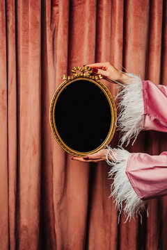 Woman's hand in nightgown holding vintage black hand mirror against pink curtains