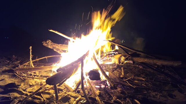 Bright bonfire burning with glowing sparks and flames on wood logs in the dark night outdoors