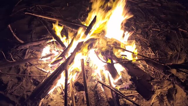 Bright bonfire burning with glowing sparks and flames on wood logs in the dark night outdoors
