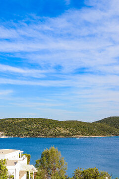 Aegean Sea bay in Bodrum, Turkey, with lush green hills, calm blue water, white resort buildings, and a clear sky