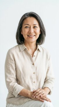 Studio portrait of a smiling mature Asian mother with grey-streaked short hair wearing a linen shirt. Ideal for family health blogs, senior lifestyle advertisements, and corporate wellness articles.