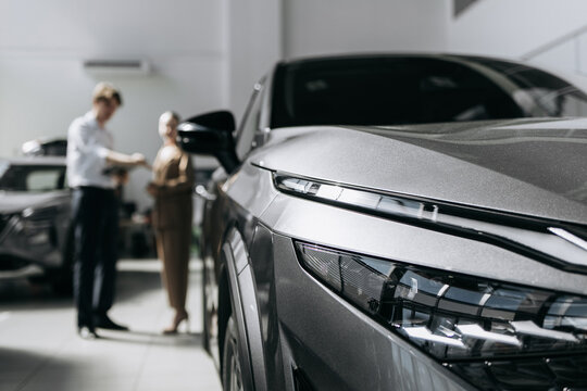 Front section of a modern car in close-up inside a dealership while customers receive consultation in the background.