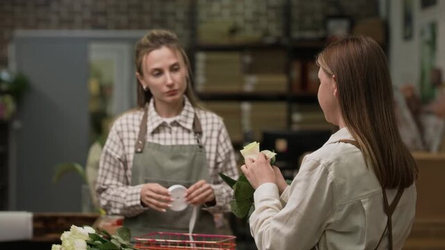 Young adult Caucasian florist training colleague in inspecting rose in wholesale flower warehouse, over shoulder shot. Footage is ideal for small business and floral industry marketing