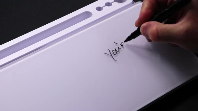 European male hand writing you&acute;re doing great on whiteboard with black pen and erases it with white sponge afterwards for seamless looping message writing on whiteboard. Positive feedback from boss.