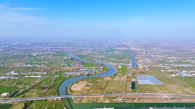 Aerial view of rural farmland and winding river near expanding city