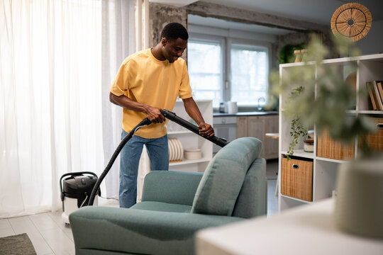 Man vacuuming sofa, cleaning home upholstery for hygiene