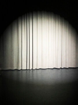 A bright spotlight illuminates a closed curtain on an empty stage