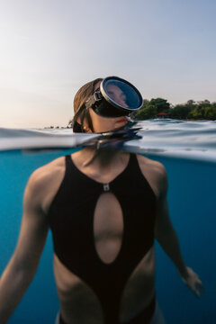 Woman snorkeling in sea water wearing diving mask, split-level underwater view with blue ocean and sunny sky