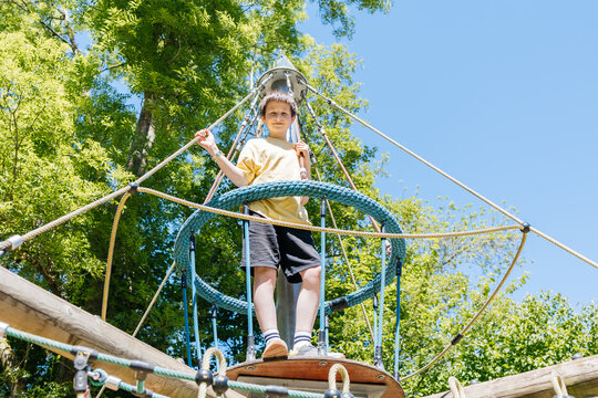 Youth in shirt playing on outdoor climbing frame looking at camera