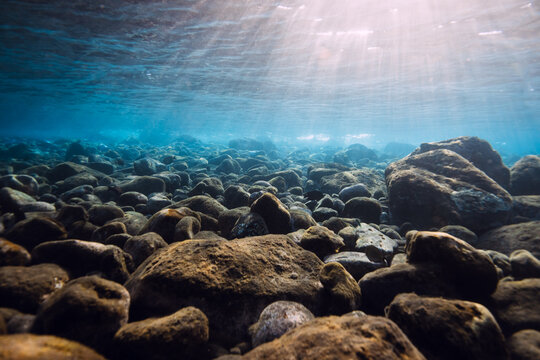 Underwater view with stones sea bottom and sun rays in blue ocean water.