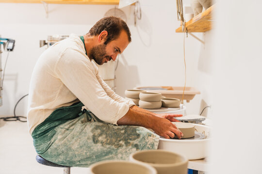 Male potter shaping clay on a wheel in his workshop