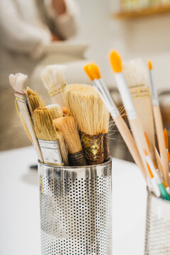 Various paintbrushes sit in a metal container in a craft studio