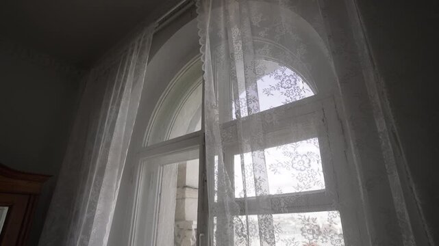 Arched interior window with lace curtains and gradually opening lower sash under soft daylight, creating nostalgic domestic mood through vertical lines, painted wood, floral texture, and airy