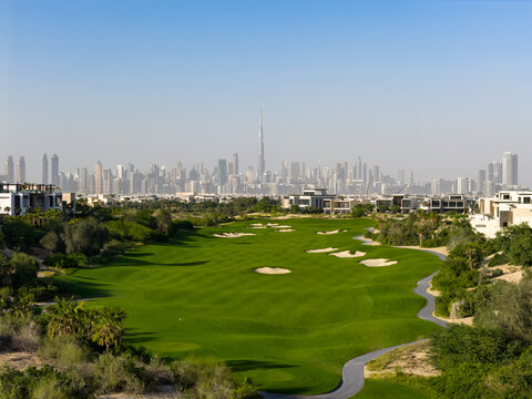 Aerial view of a lush green golf course with sand bunkers and a winding path, featuring the Burj Khalifa and Dubai skyline in the background in Dubai, Dubai, United Arab Emirates.