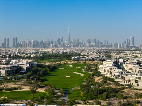 Aerial view of the Burj Khalifa and the Dubai skyline rising above a lush green golf course and modern residential villas in Dubai, Dubai, United Arab Emirates.
