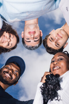 Smiling men and women look down at camera forming a circle outdoors