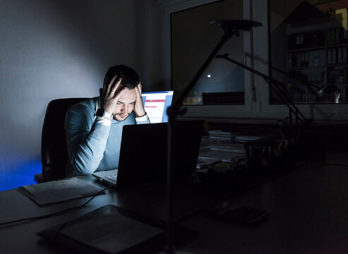 Tired businessman sitting at desk in office at night