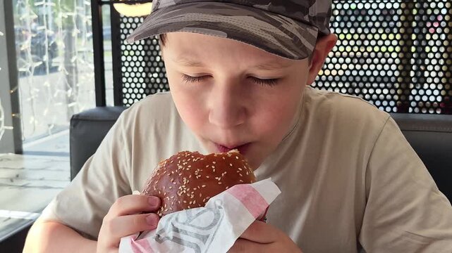 A close-up of a bite of a burger. Boy eating a large sesame burger in a fast food restaurant, casual dining, tasty meal, teenage lifestyle, food enjoyment