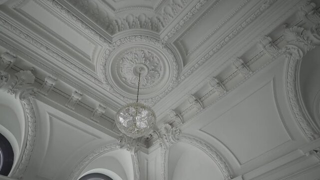 Crystal chandelier descending beneath ornate plaster medallion inside elegant historic interior, with ceiling ornament, carved molding, arch detail, sparkling crystal reflections and refined symmetry