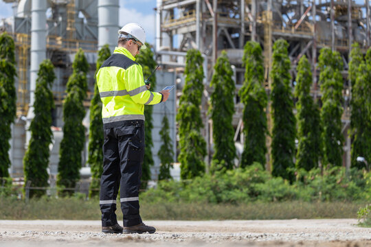 Oil refinery engineer using digital tablet at industrial plant site, Petroleum plant worker in safety gear checking tablet outdoor, Energy industry professional inspecting facility