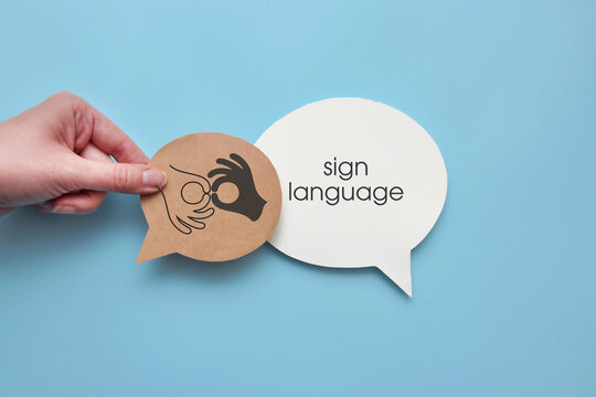 Hand holding a speech bubble with a sign language symbol next to a larger speech bubble labeled &ldquo;sign language,&rdquo; representing visual communication and accessibility.