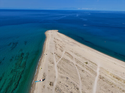 Aerial view of the sandy cape of Possidi surrounded by turquoise and deep blue Aegean Sea waters under a clear sky in Possidi, Greece.