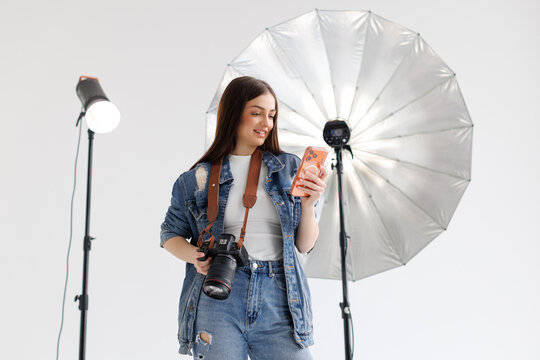 Smiling beautiful woman photographer holding manual camera and use phone while sitting at her working place.