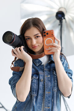 Smiling beautiful woman photographer holding manual camera and use phone while sitting at her working place.