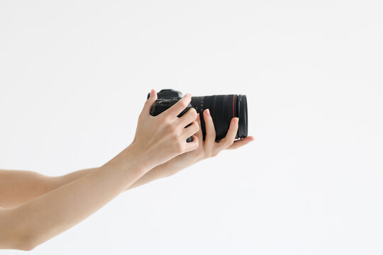 Human hand firmly holds professional camera with lens hood pointing forward on white background
