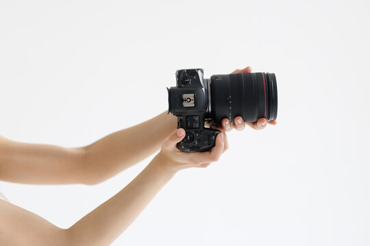 Human hand firmly holds professional camera with lens hood pointing forward on white background