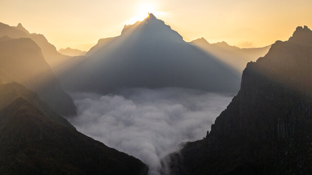 Aerial view of Gunung Kelud at sunrise with golden sun rays illuminating the peak and a thick sea of clouds filling the volcanic crater in Kecamatan Ngancar, Jawa Timur, Indonesia.