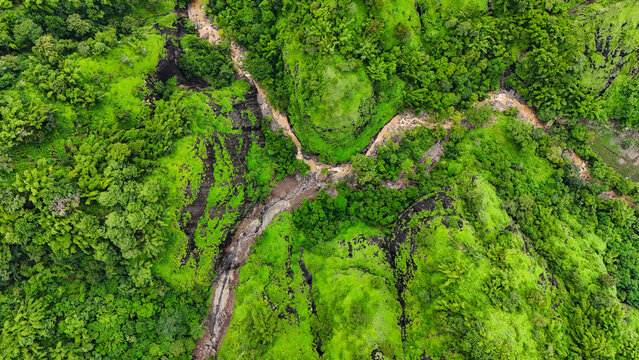 Aerial view of the lush green tropical landscape with a winding river cutting through dense vegetation and rocky terrain near Pantai Loji Pelabuhan Ratu in Palabuhanratu, West Java, Indonesia.