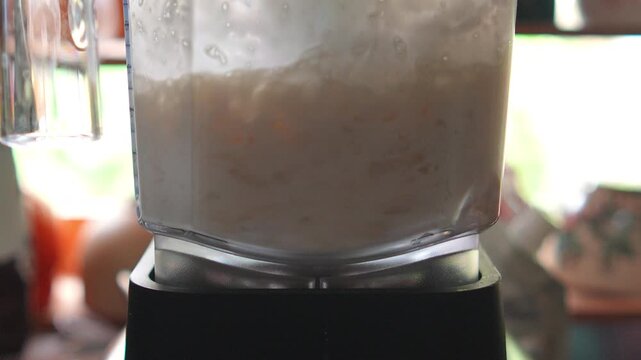 4K Electric blender blending ice and ingredients inside clear pitcher, refreshing crushed ice smoothie or cold drink recipe in cafe kitchen setting.