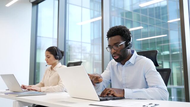 Team of corporate operators working in customer support service on helpline telesale using laptop. Two call center agents in headsets, men and women helping online, answer questions sitting in office