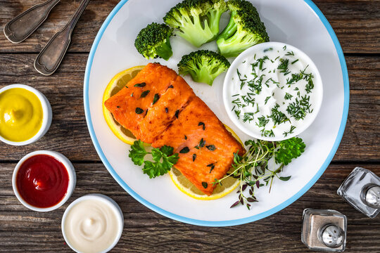 Fried salmon steak with boiled broccoli and dill yogurt sauce on wooden table. Top view
