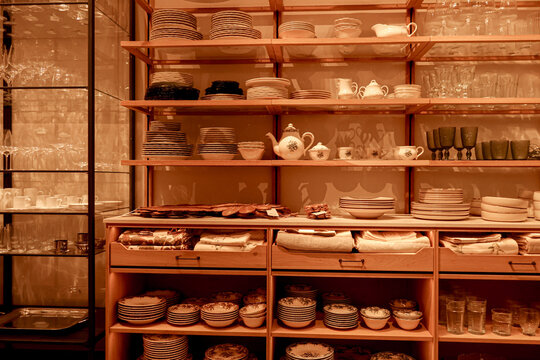 Store interior showcasing a variety of ceramic plates, bowls, cups, and elegant glassware along with folded textiles on wooden shelves