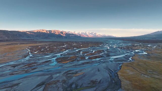 Aerial sunrise over braided river valley and snow-capped mountains