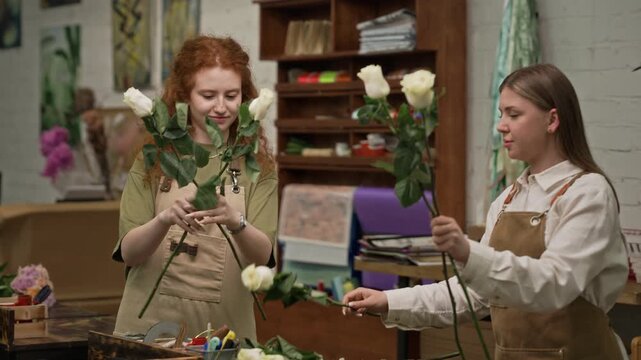 Two young Caucasian female florists wearing aprons sorting and arranging fresh roses in flower workshop. Footage is perfect for small business marketing and floral industry promotions