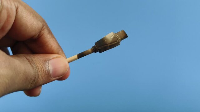 Hand holding cheap quality faulty or defective smartphone type c charging cable with burn damage. Short circuit, power surge, electricity overload, high voltage accident or fire hazard risk concept.