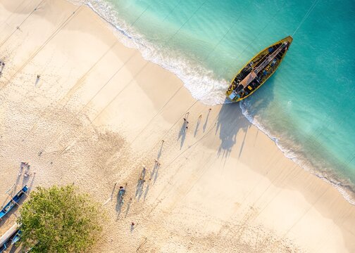 Aerial view of Papuma Beach with a yellow boat resting on the white sand, turquoise water, and people walking along the shoreline in Jember, East Java, Indonesia.