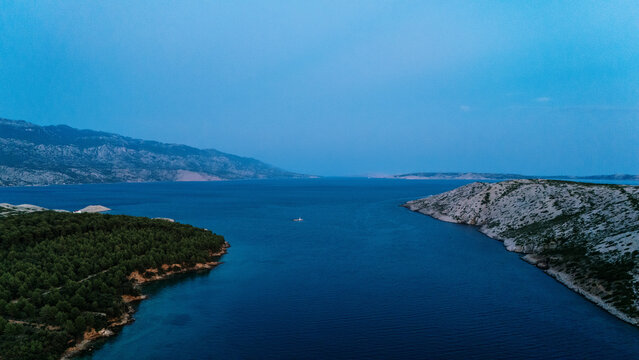 Aerial view of the coastline of Rab island featuring dense pine forests, rocky cliffs, and the deep blue waters of the Adriatic Sea in Rab, Primorje-Gorski Kotar, Croatia.